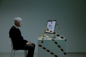 elder man sitting in front of a computer tied with black and yellow tape